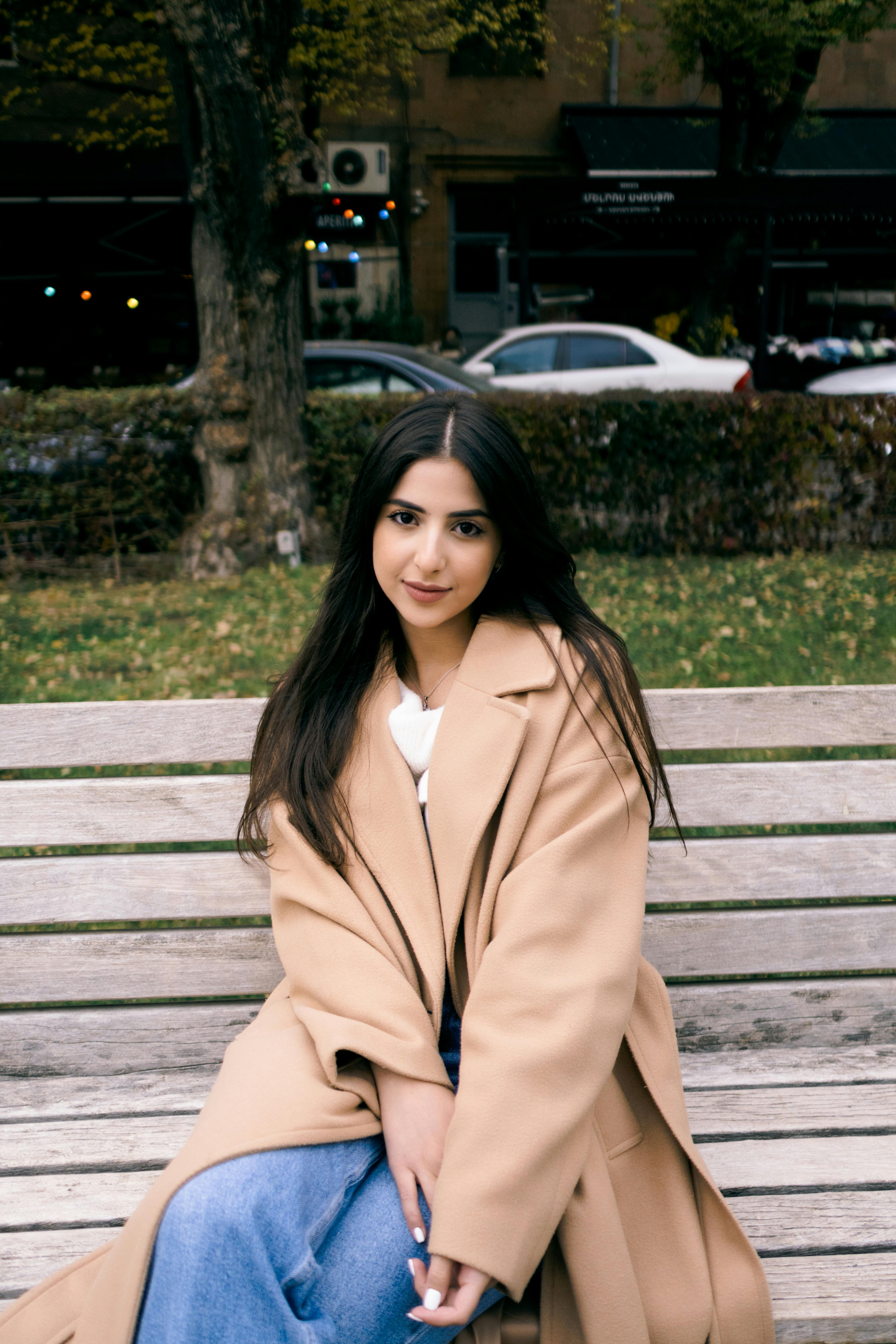 Stylish woman in a brown coat sits on a park bench in Yerevan, Armenia.