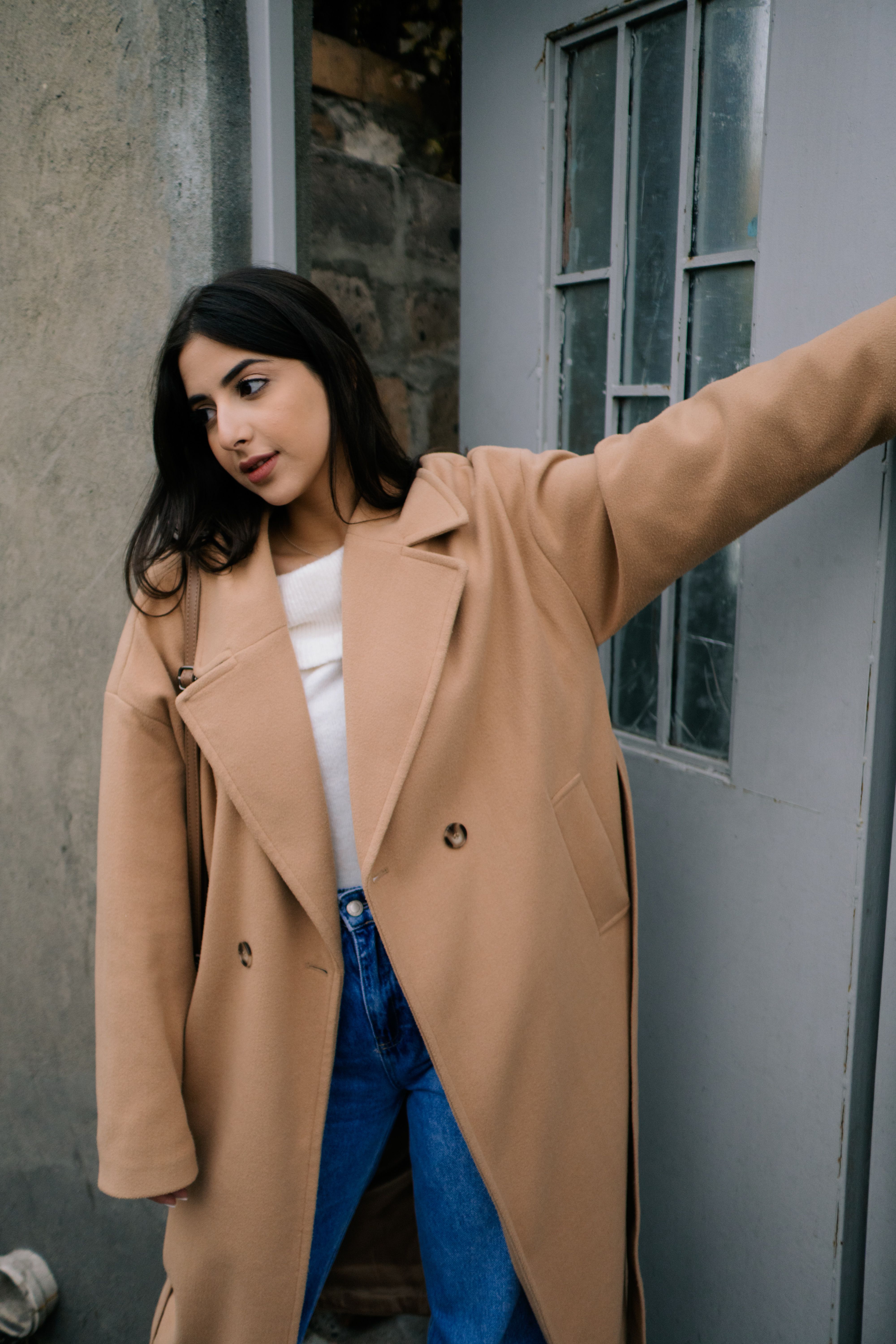 Woman in Brown Coat Standing Near White Wall · Free Stock Photo