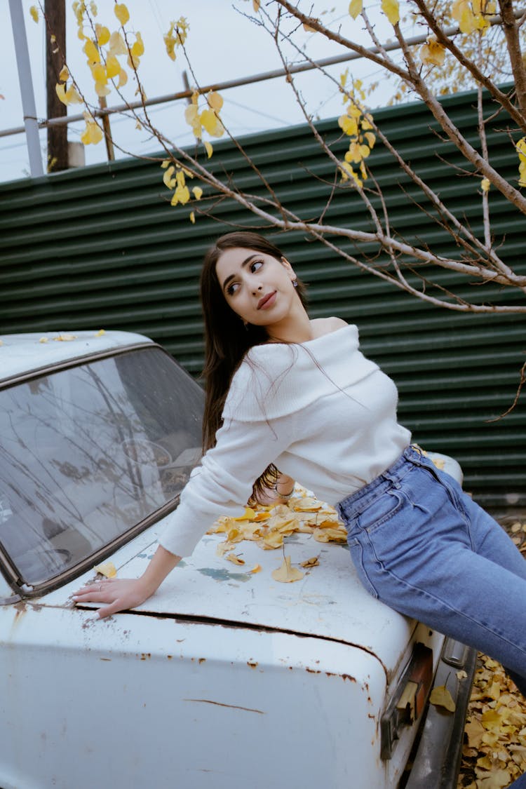 Young Woman In White Off Shoulder Sweater Posing And Leaning On A Vintage Car