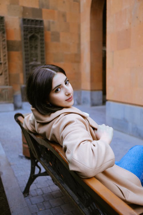 Young Woman in Beige Coat Sitting on an Outdoor Bench