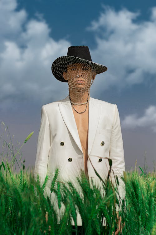 Man in White Suit Wearing Brown Hat Standing on Green Grass Field