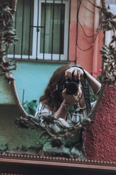 A woman capturing her reflection with a camera in a decorative mirror outdoors.