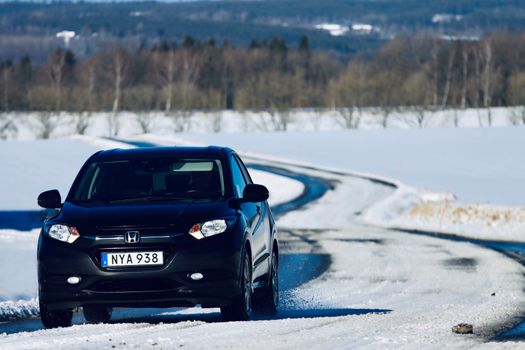 A black car navigating a winding snowy road during winter, surrounded by a scenic landscape.