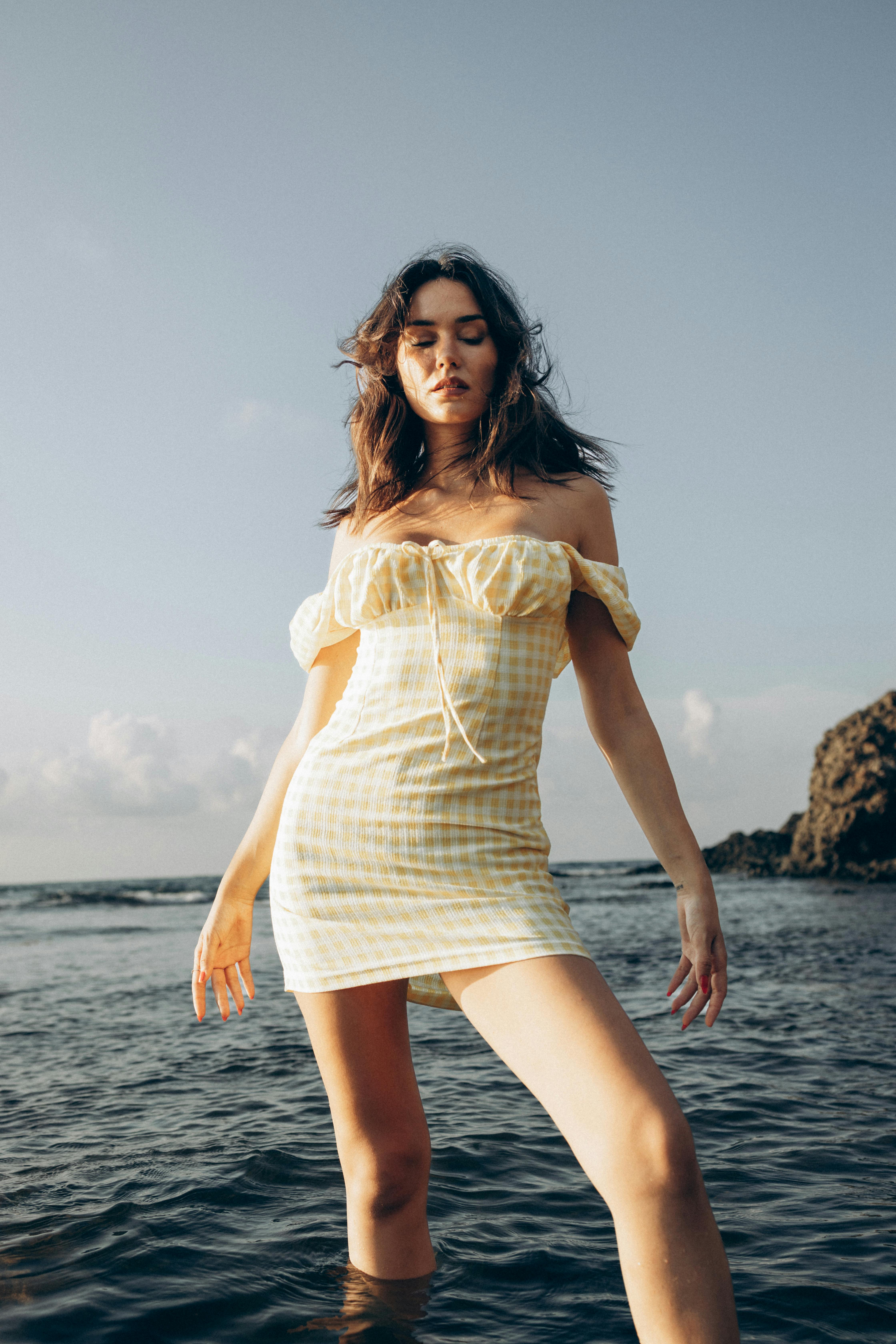 一位时尚的女士穿着格子连衣裙在海岸线上摆姿势，在宁静的环境中反映出夏季的时尚