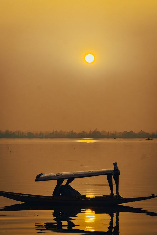Free Silhouetted boat gliding on a tranquil river at sunset with golden sky and reflections. Stock Photo