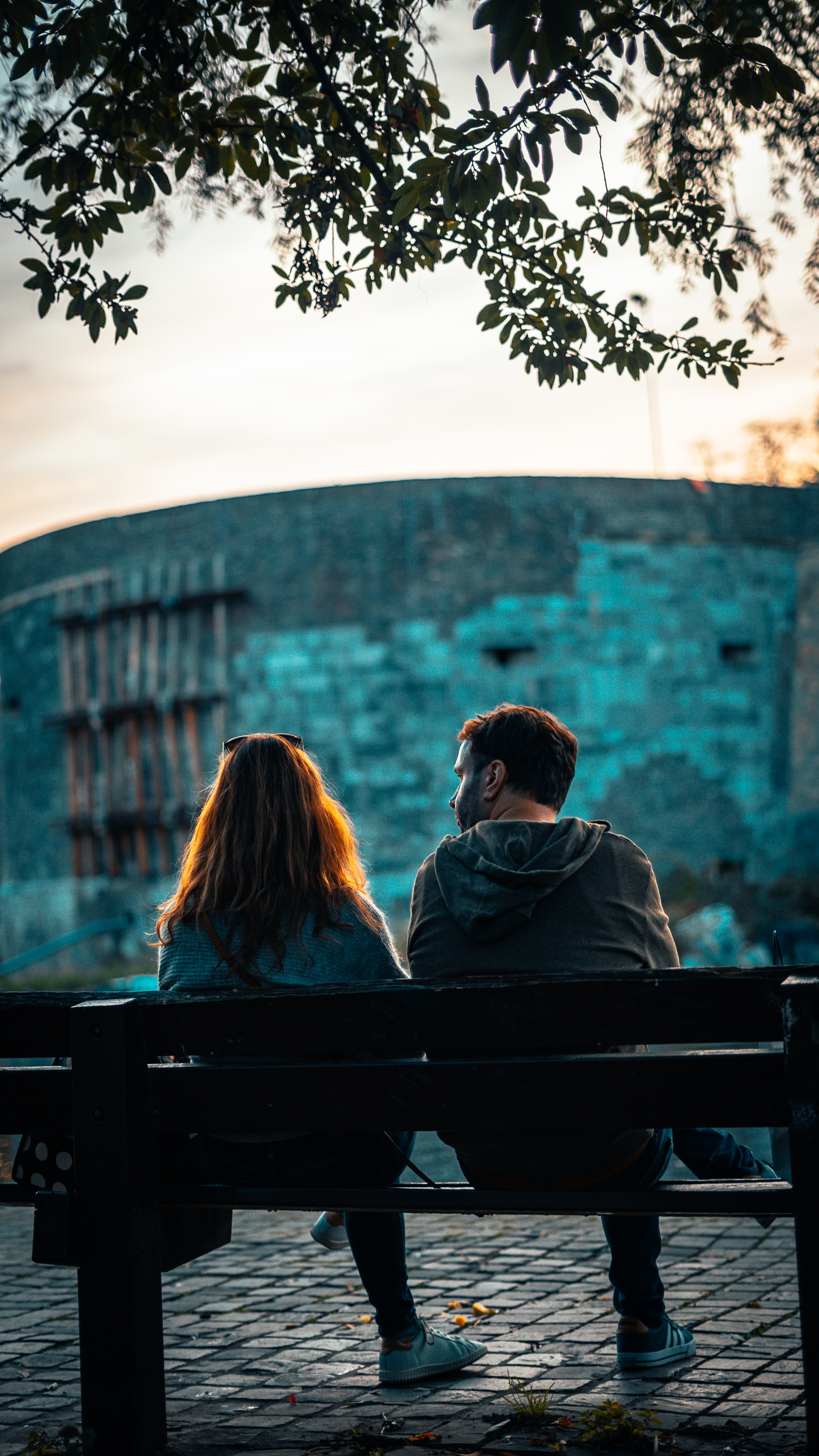 A couple sitting romantically on a park bench in Maastricht, surrounded by historic architecture and nature.