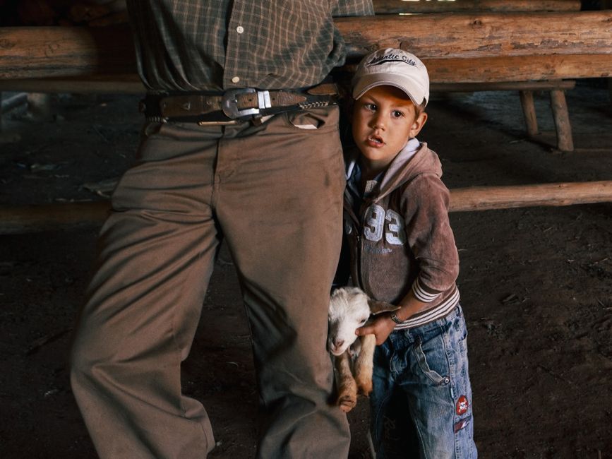 Un niño pequeño se aferra a un adulto mientras sostiene un cabrito en el interior.