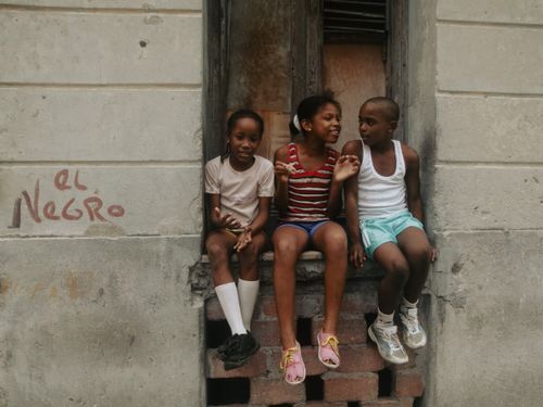 Free Three kids sitting on a window ledge, enjoying a casual day in the city. Stock Photo