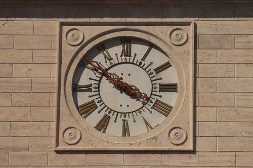 Free Close-up of a vintage wall clock with Roman numerals on a beige brick background. Stock Photo