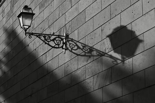 Free Black and white image of a street lamp casting an intricate shadow on a brick wall, capturing urban elegance. Stock Photo