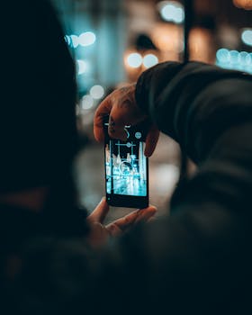 Close-up of a person photographing city lights at night in Kutaisi, Georgia using a smartphone.