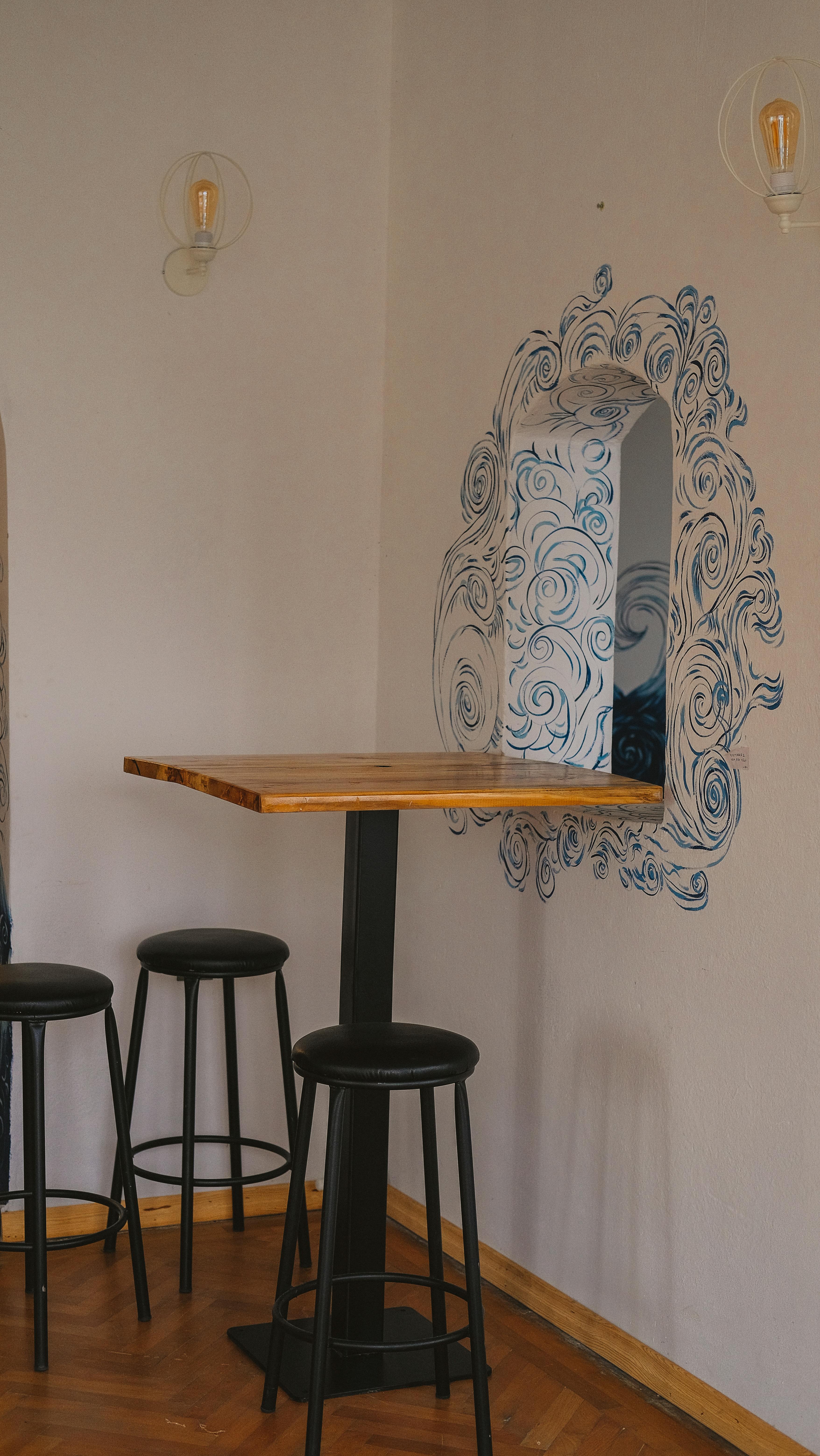 Free Cozy café corner featuring a high wooden table and artistic wall designs, perfect for urban interiors. Stock Photo