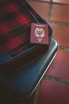 Red plaid suitcase with Venezuelan passport on a tiled floor, conveying travel symbolism.