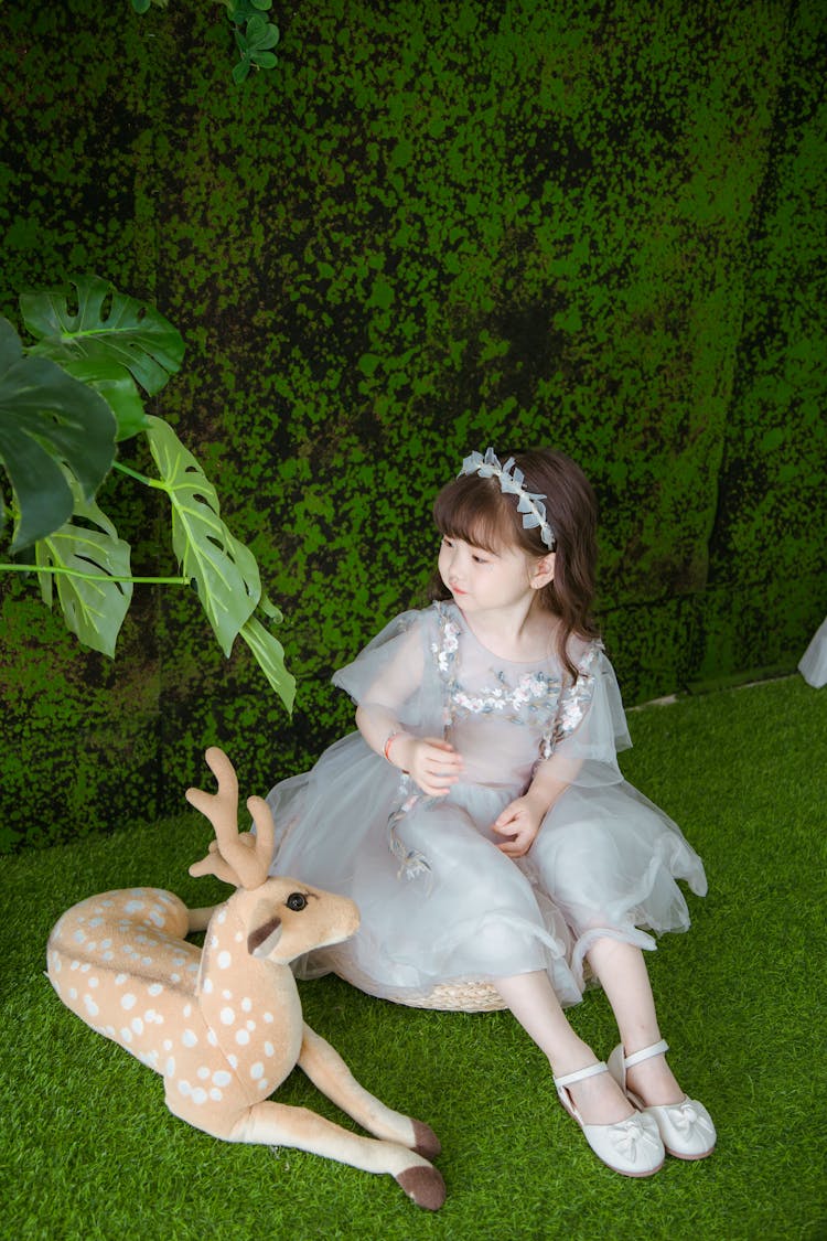 Girl In Dress Sitting With Toy Deer