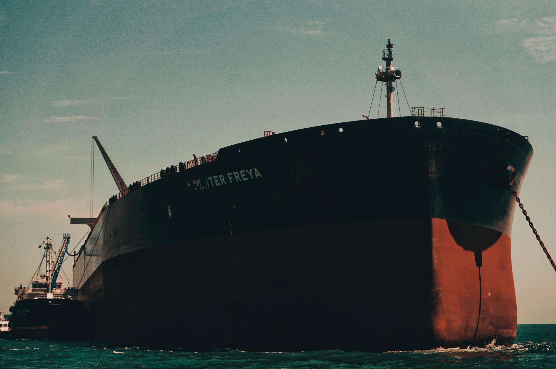 A massive cargo ship named Hunter Freya anchored at a bustling sea port under a clear sky.