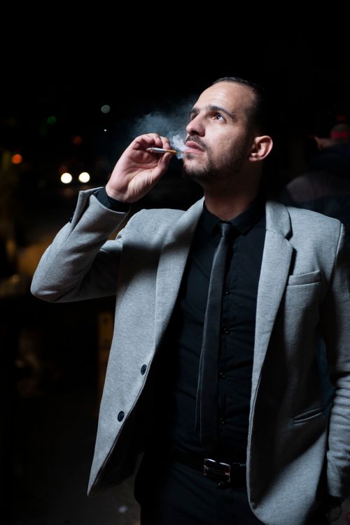 Free A stylish businessman in a gray suit smokes at night on the streets of Paris, France. Stock Photo