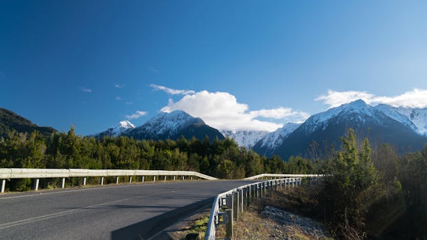 A picturesque road view with lush greenery and snowy mountains in the backdrop.