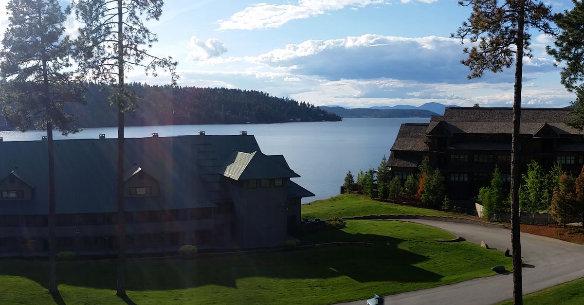 Panoramic view of a beautiful waterfront resort with buildings by the lake and tall trees under a summer sky.