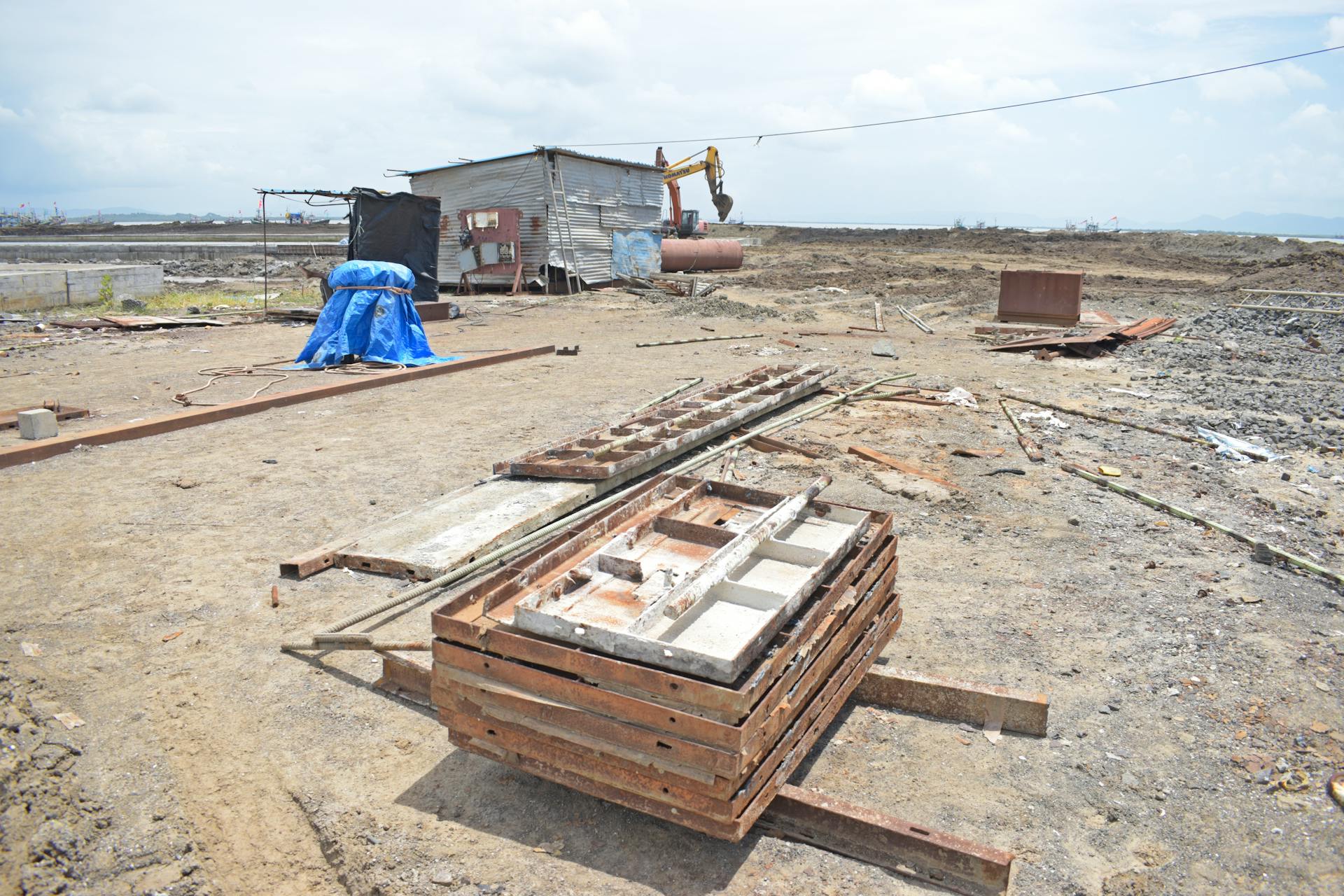 Abandoned construction site with excavator and debris under a bright sky.