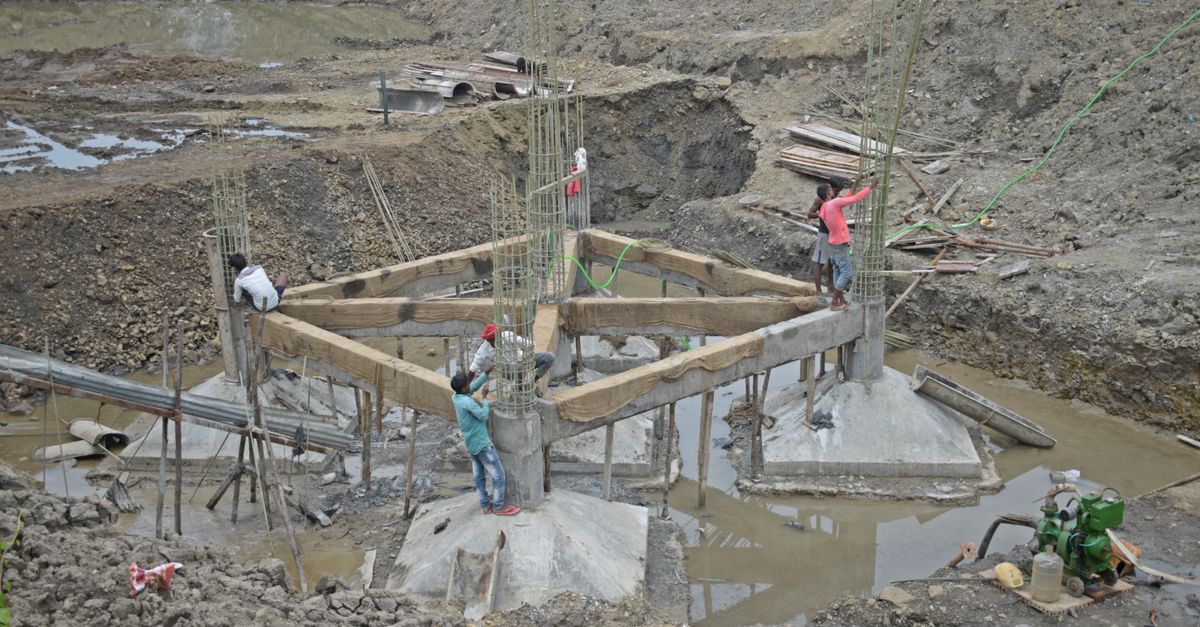 Workers constructing a building foundation with rebar and wooden supports outdoors.