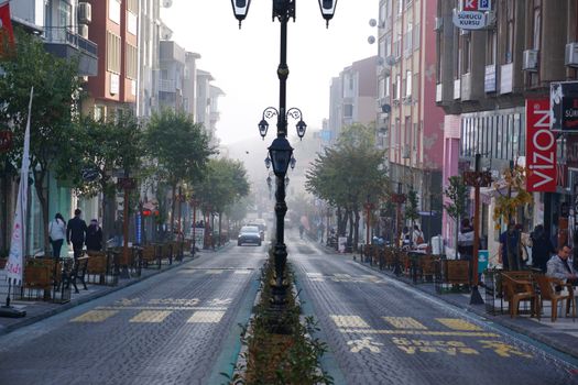 Foggy morning view of an urban street with buildings, cars, and cafes.