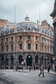 Elegant historic building in London's financial district with people walking by on a cloudy day.