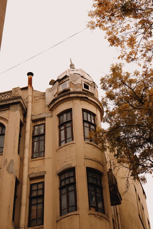 Free An old, worn building with architectural details amidst autumn trees, showcasing urban decay. Stock Photo