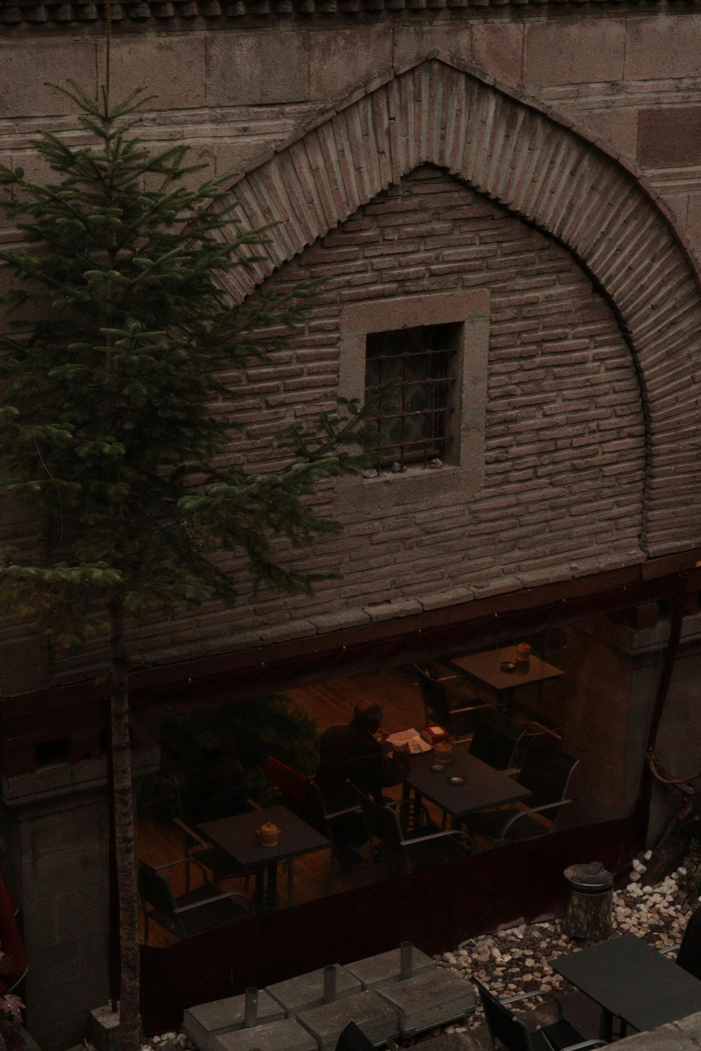 Free A cozy outdoor café scene beneath a rustic stone arch, capturing a quiet ambiance. Stock Photo