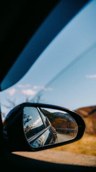 Side mirror captures a scenic road trip view, highlighting travel and adventure themes.