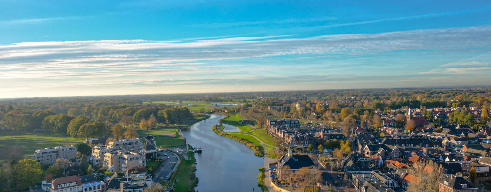 Stunning aerial view of Ommen, Nederland with the River Vecht winding through the landscape under a bright blue sky.