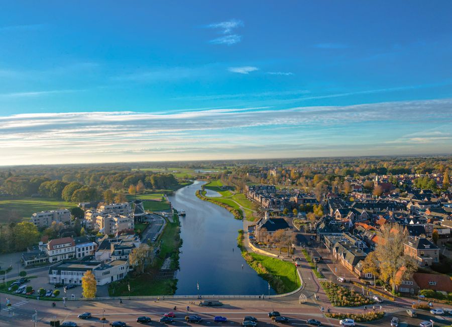 Stunning aerial view of Ommen, Nederland with the River Vecht winding through the landscape under a bright blue sky.