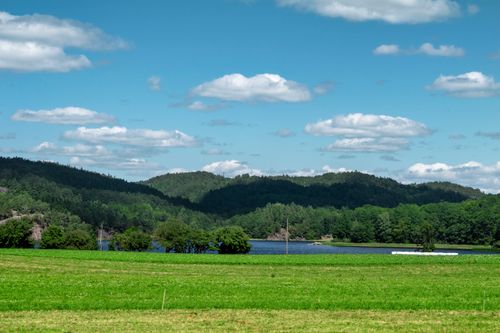 Free A beautiful landscape featuring a lush green field, blue sky, and distant hills under a bright sunny day. Stock Photo