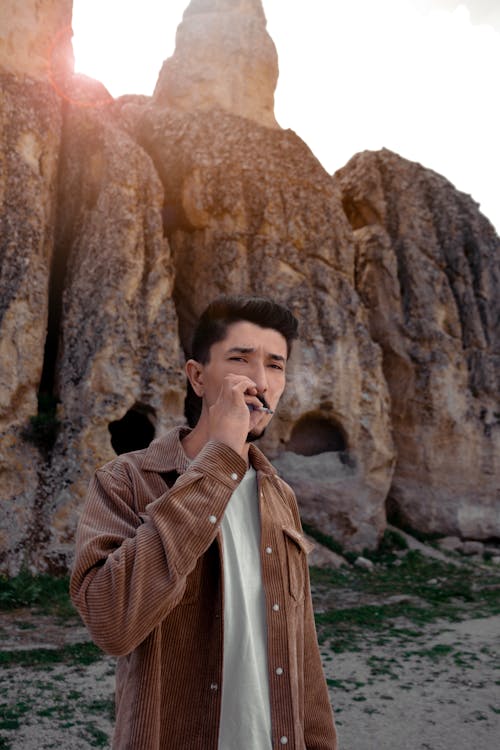 Мужчина курит возле скалы на закате