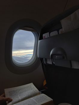 Passenger reading a book on a flight over Thessaloniki with a view out the airplane window.
