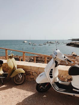 Colorful scooters parked by a stone wall overlooking the blue Mediterranean sea and boats on a sunny day.