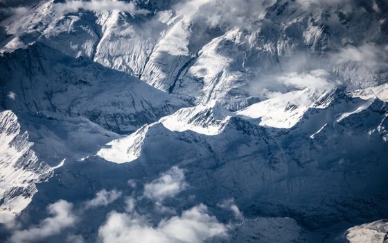 Breathtaking aerial photograph of snow-covered mountain range with peaks and clouds.