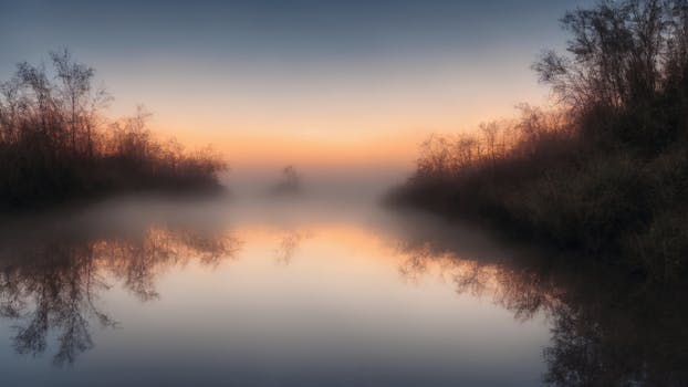 Serene sunrise over a misty lake surrounded by trees reflecting in calm water.