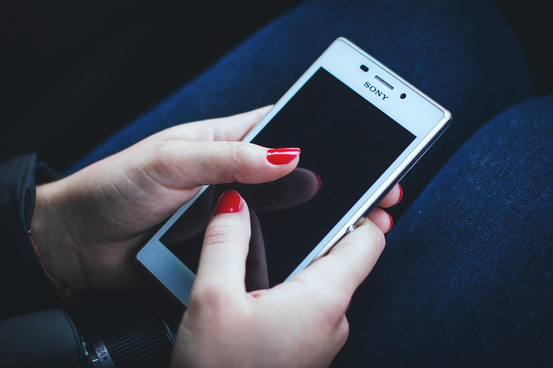 Person with red nails using a smartphone, focusing on the screen and touch interaction.