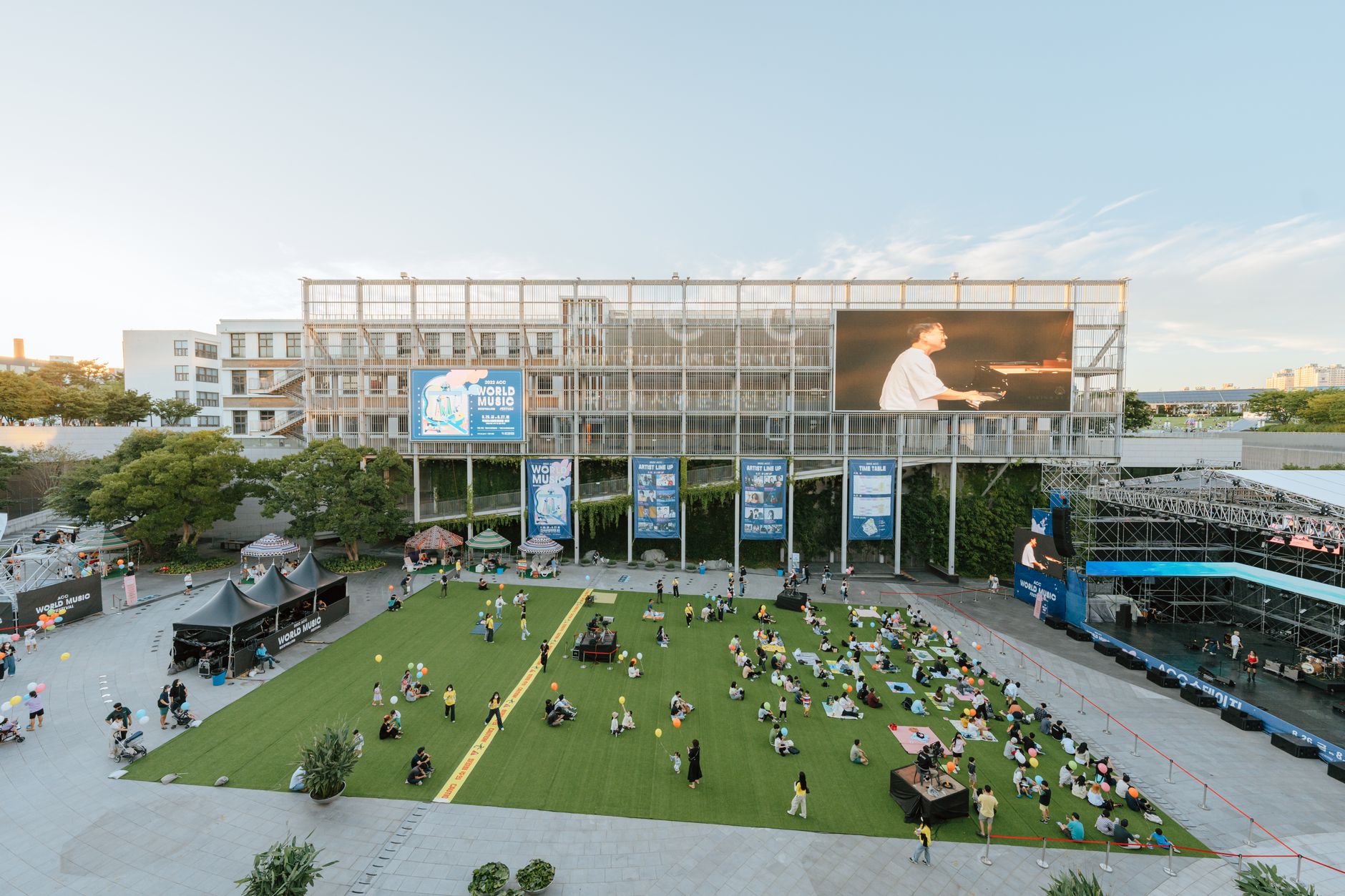 A vibrant outdoor concert at the Asia Culture Center plaza with an audience enjoying sunset views.
