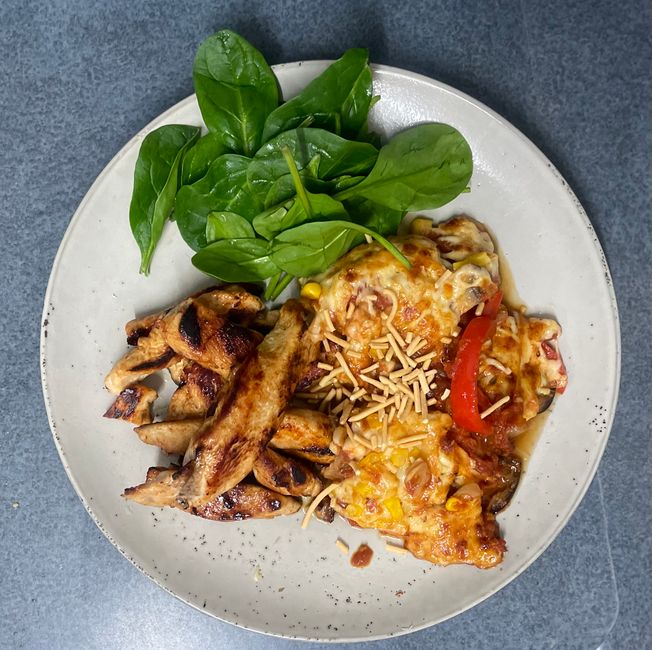 A baking dish of Santa Fe chicken breasts topped with melted cheese, black beans, corn, and diced tomatoes, garnished with cilantro and lime wedges.