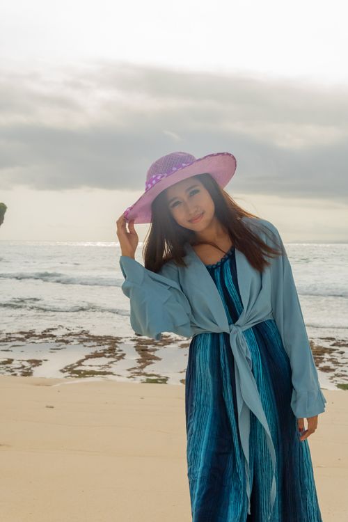 Free Asian woman in blue attire with a purple hat enjoys a beach day in Bali. Stock Photo