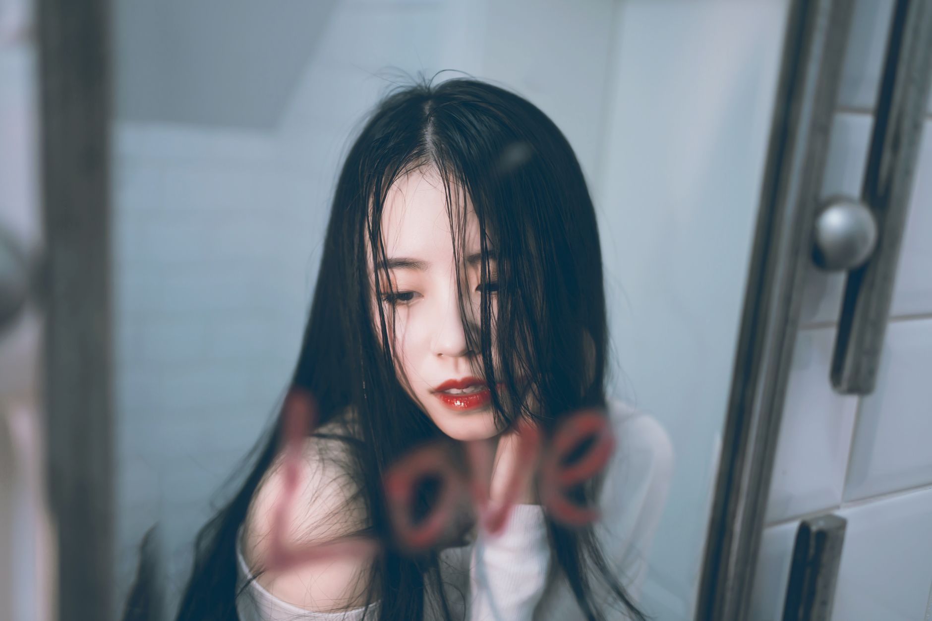 Close-up portrait of a woman with red lips and long hair in front of a mirror with 'love' written on it.