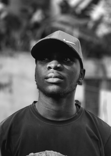 A striking black and white headshot of a man wearing a cap, with a thoughtful expression.