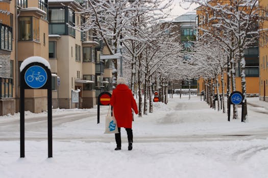 A woman in a red coat walks through a snowy urban street in Sweden.