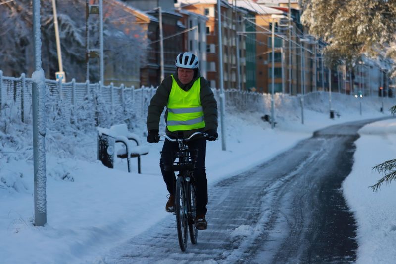 A cyclist in a safety vest rides on snow-covered streets during winter, promoting safe outdoor activity.