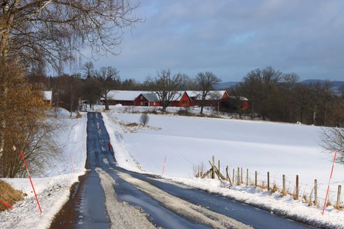 Free A picturesque winter road with red barns and snow-covered fields under a cloudy sky. Stock Photo
