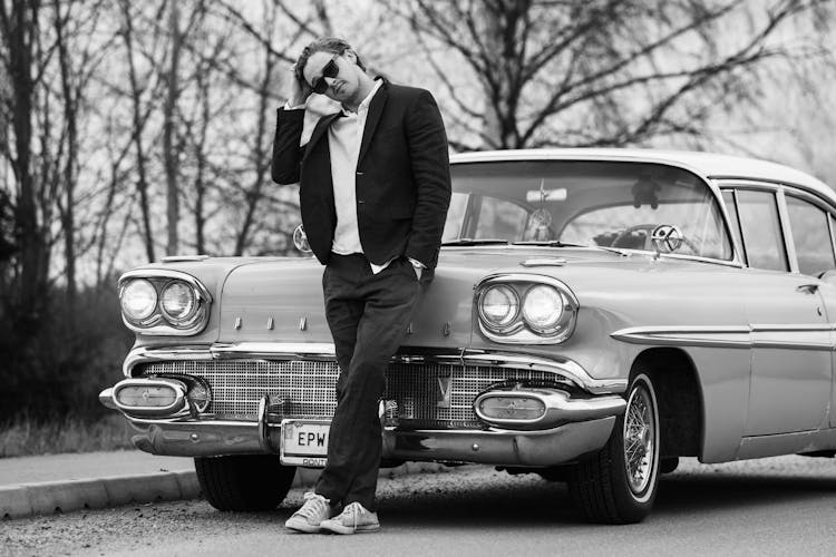 Grayscale Photo Of A Man Posing In Front Of A Pontiac Car