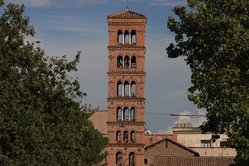 Free A classic red brick bell tower amidst lush greenery and urban landscape. Stock Photo