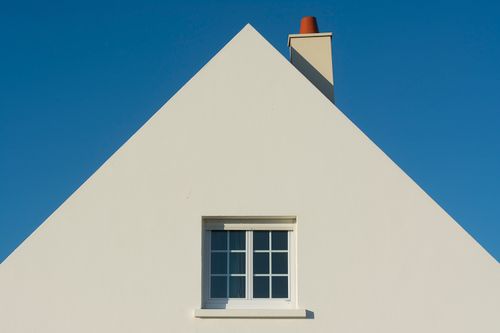 Free Simple triangular house facade with window and chimney against a clear blue sky. Stock Photo