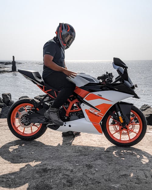 Man in Black T-shirt and Black Helmet Riding on an Orange Sports Bike Near Beach